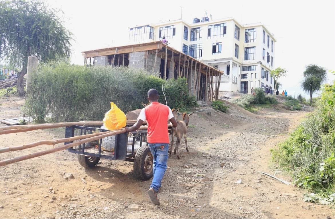 Una persona lleva una carretilla por un camino junto a edificios en Mbita.