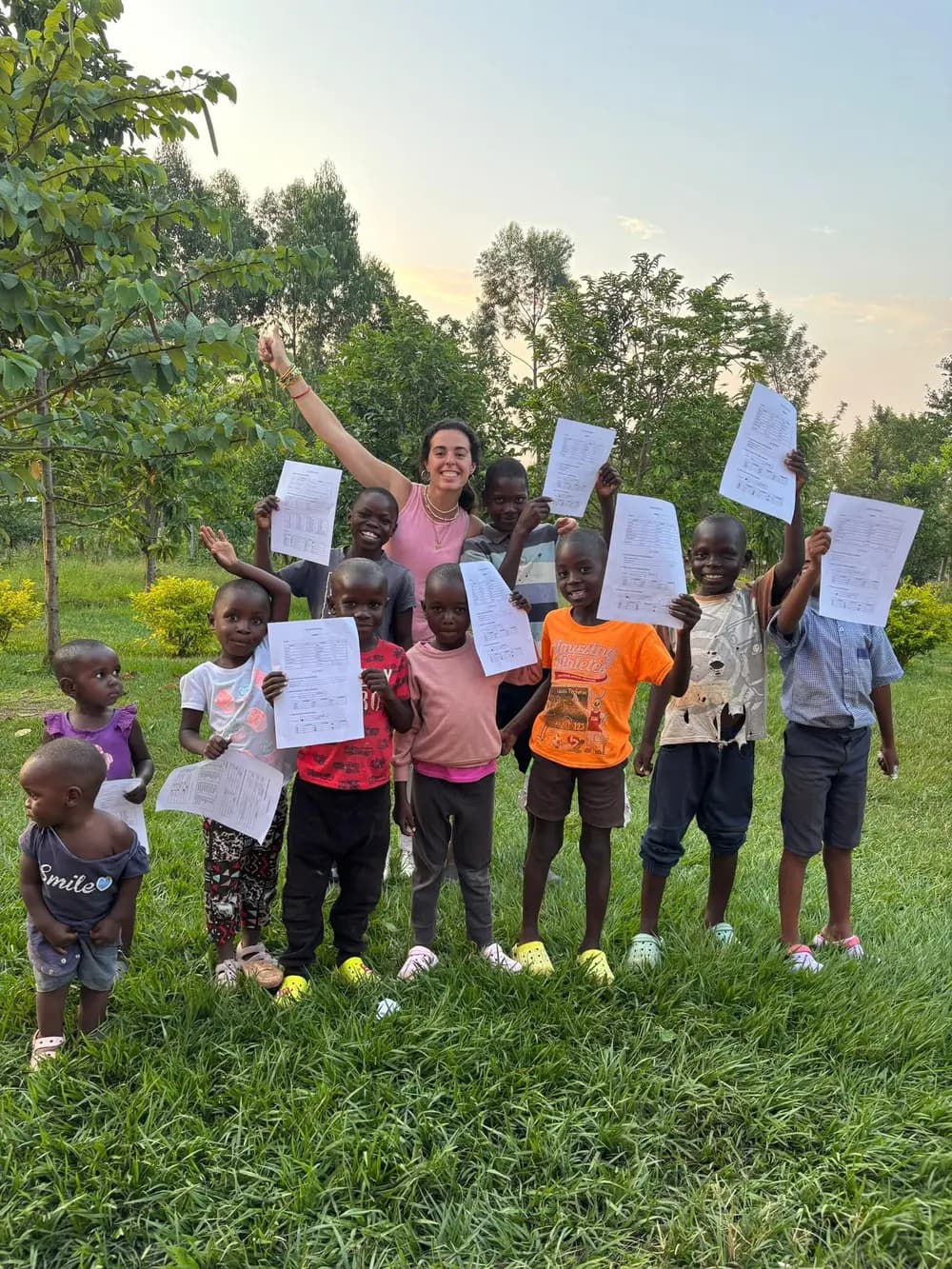 Un grupo de niños y una mujer sonríen al aire libre mientras levantan unas hojas.